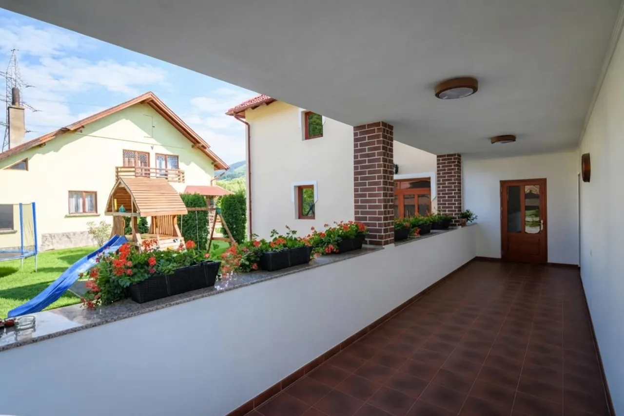 Terasă acoperită cu jardiniere, cu vedere spre grădină și locul de joacă